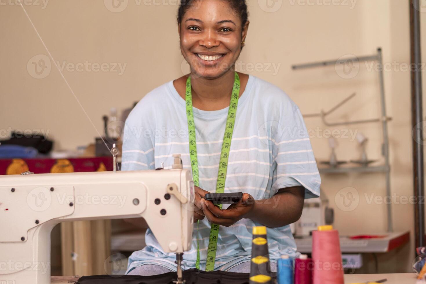 cute female dressmaker using her phone while working with sewing machine photo