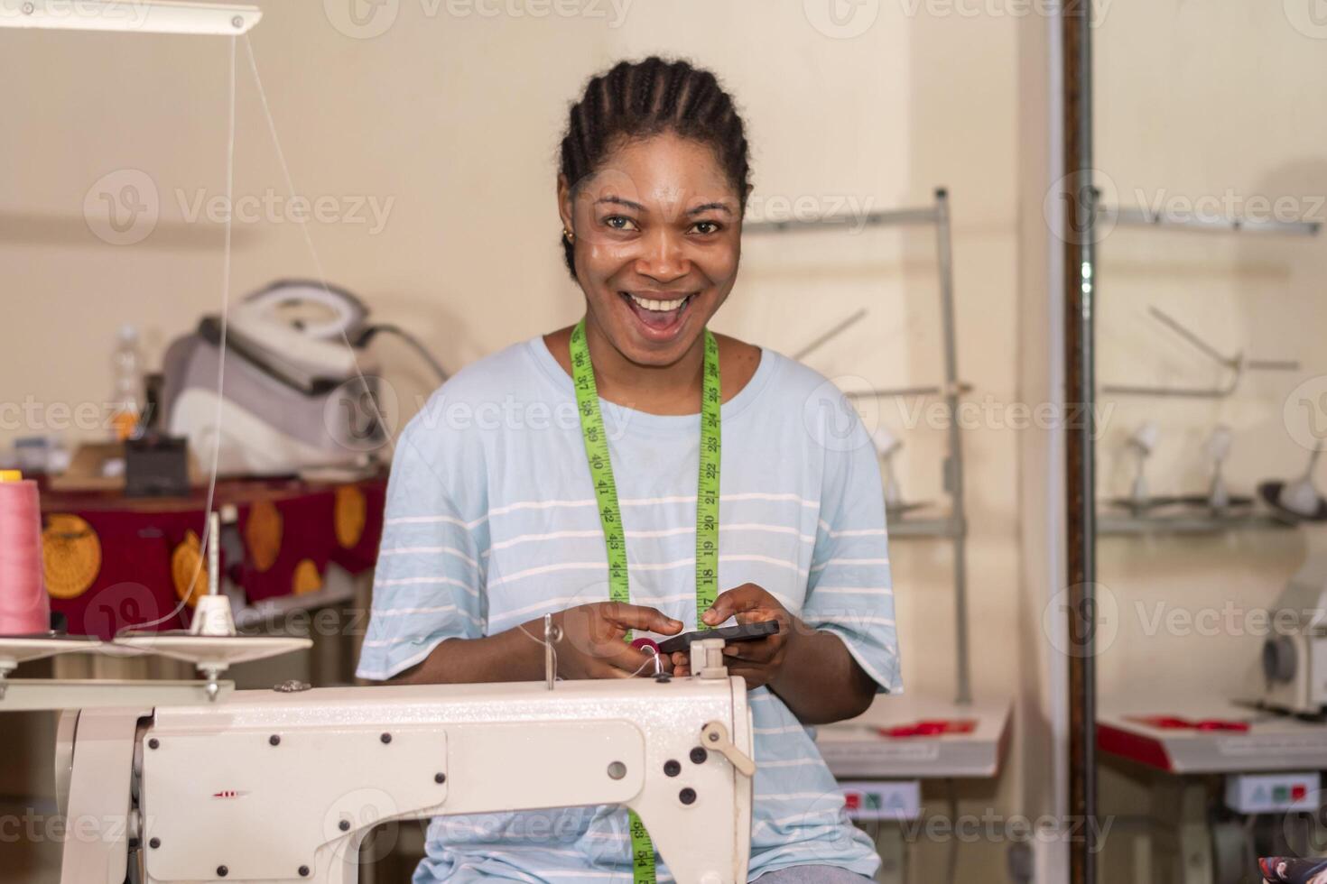 focused female dressmaker using her phone while working with sewing machine photo