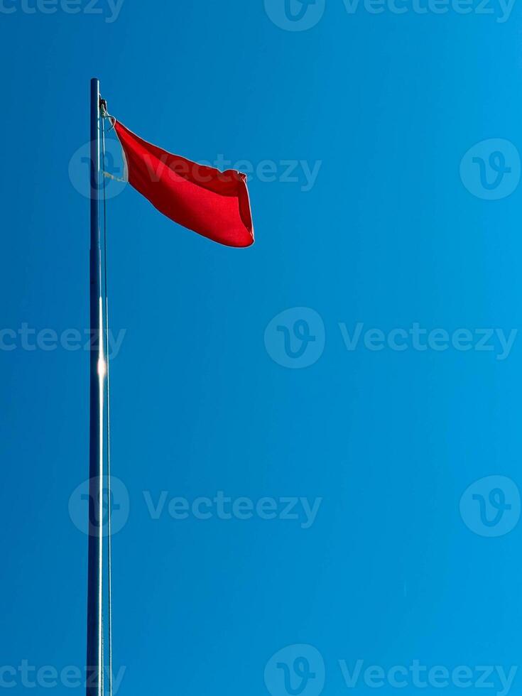 A red flag flutters in the wind in the blue sky by the sea during the day. photo