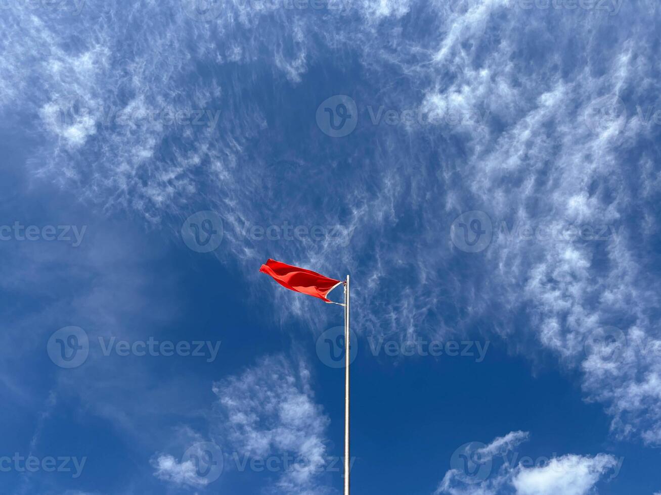 A red flag on a pole flutters in a strong wind in the blue sky. photo