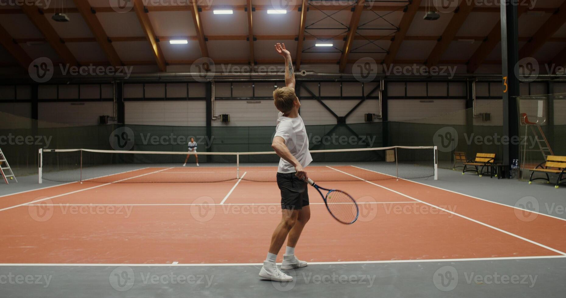 Young man and woman, play tennis on an indoor tennis court, throwing the ball with a racket over the net photo