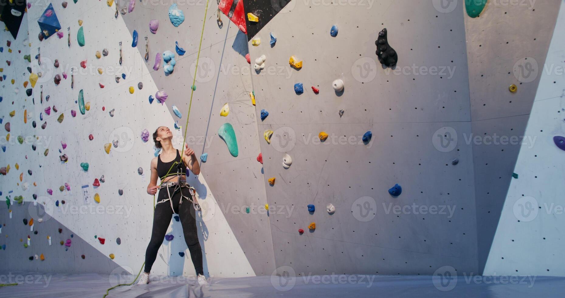 A young woman pulls on safety rope for a man descending from a climbing wall while standing at the foot of the wall. limbing workout on an artificial surface in the indoor gym photo