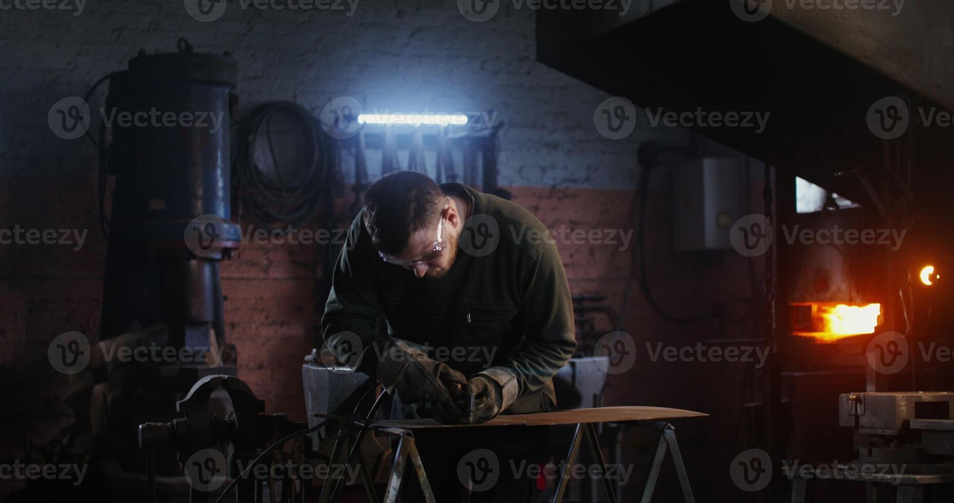 Young man of European appearance, dressed in work clothes and goggles, cuts a sheet of iron with a plasma cutter, working in a forge, sparks fly in different directions. 4k, red komodo photo