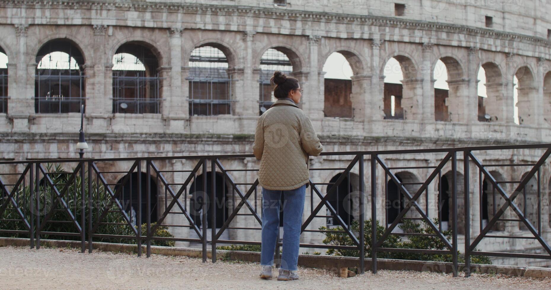 A young warmly dressed Caucasian woman smiles as she takes in the sights of Rome from observation deck near the Coliseum. in 4k, red komodo. photo