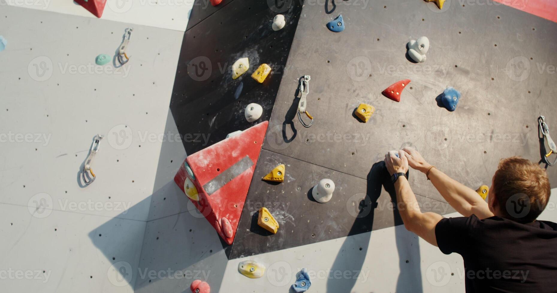 A young man of European appearance slowly and concentratedly climbs up the climbing wall without safety ropes photo
