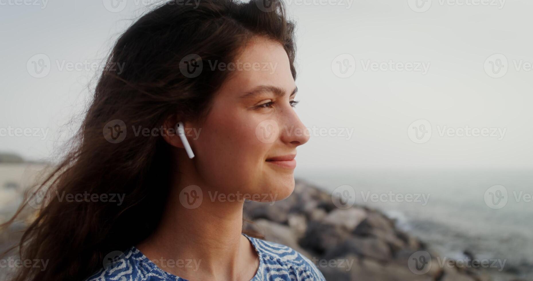 Beautiful young woman with flowing curly dark hair with wireless headphones in her ears photo