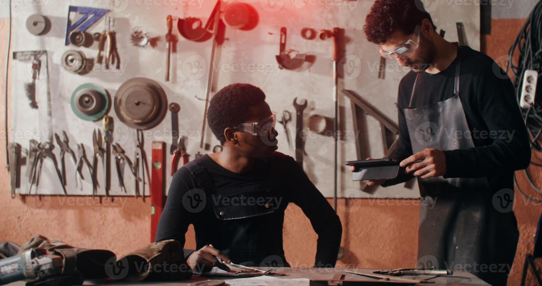 Male blacksmith in work clothes shows his colleague an idea for a sketch on a clipboard, working together to design a future product in a workshop full of tools. in 4k, red komodo photo