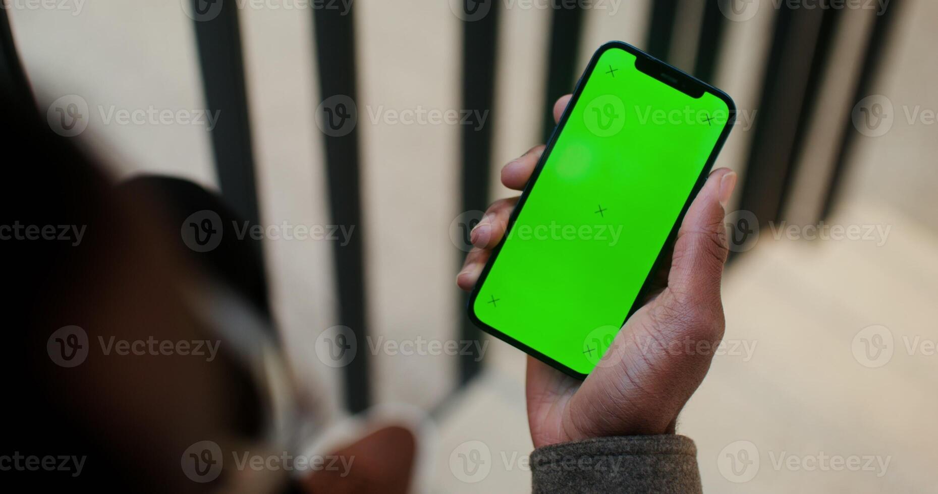 Mobile phone with a green screen in the hand of a man of African American appearance, filming from behind, his face is not visible. Copy space, mockup, chroma key. in 4k, red komodo photo