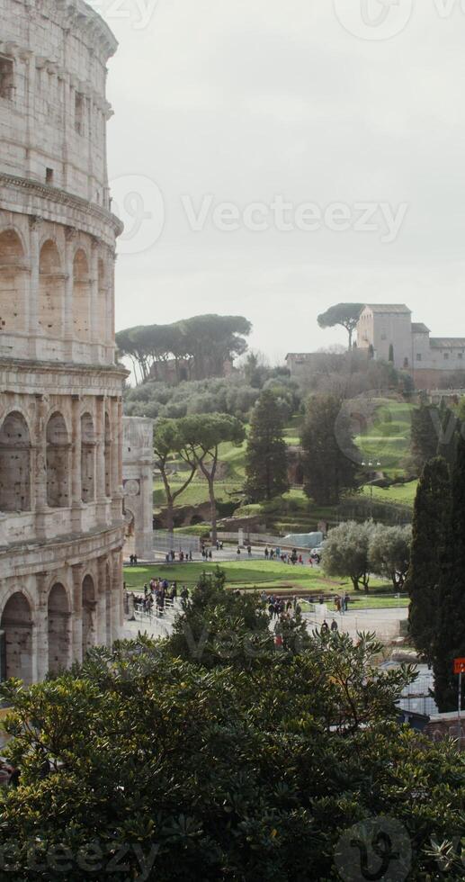 The side of Colosseum and the area in front of the attraction filled with tourists on a sunny clear day. Italy Rome. in 4k, red komodo, vertical photo