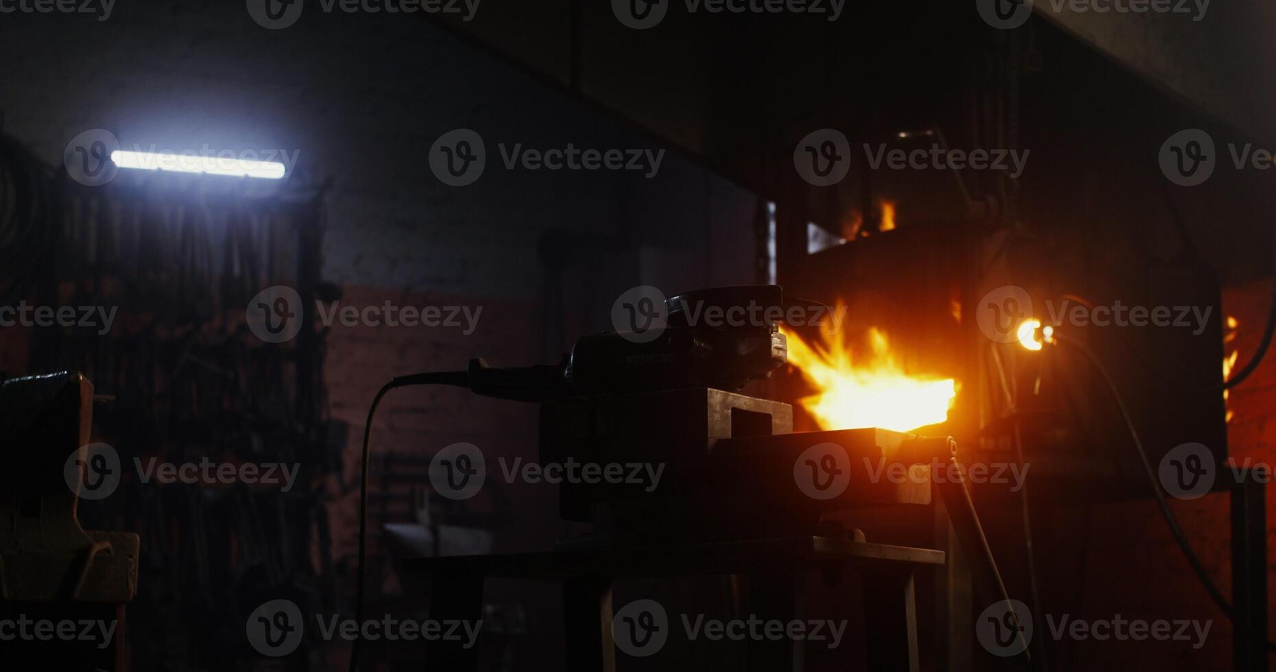 Blacksmith in protective gear and goggles takes an angle grinder and starts to cut off a part of a metal blank while working in a forge. 4k , red komodo photo
