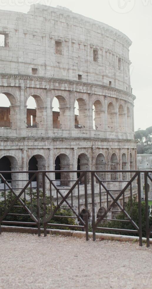 Young warmly dressed woman comes to the observation deck in front of the Coliseum and stops looking at the amphitheater. Italy Rome. in 4k, red komodo, vertical photo