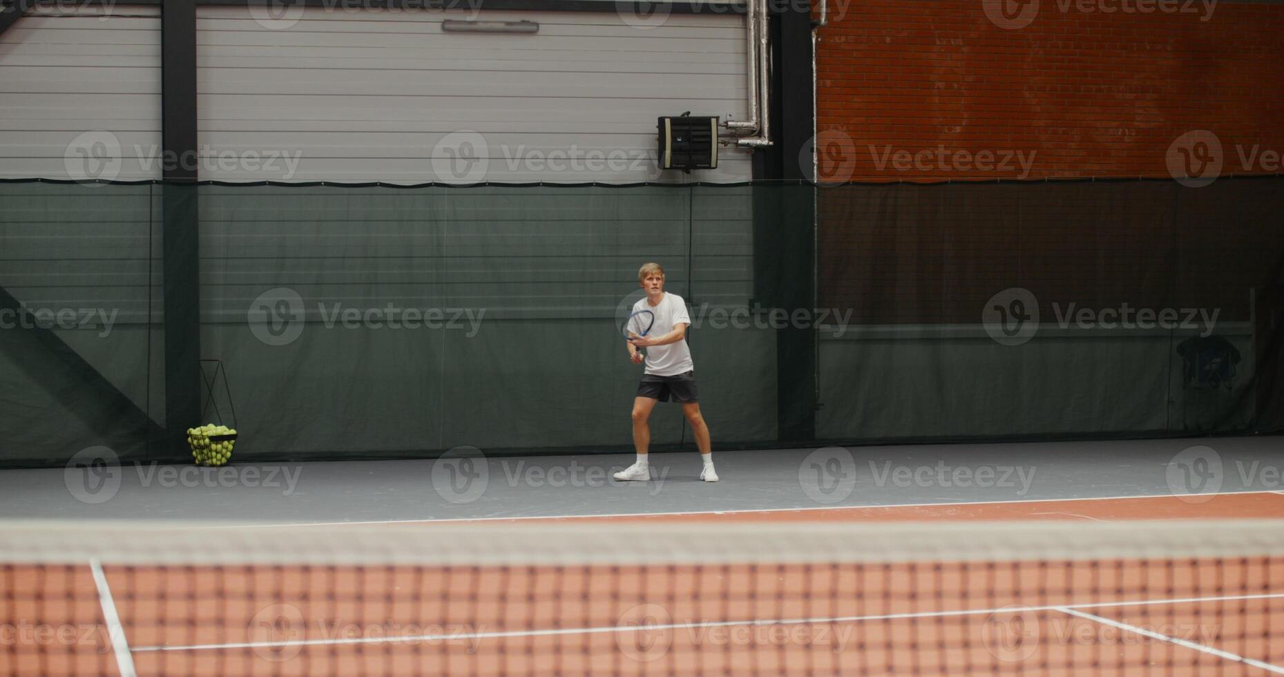 Young man of European appearance, dressed in a stylish sports uniform, serves the first ball, starting a long tennis set, actively moving and hitting the ball photo