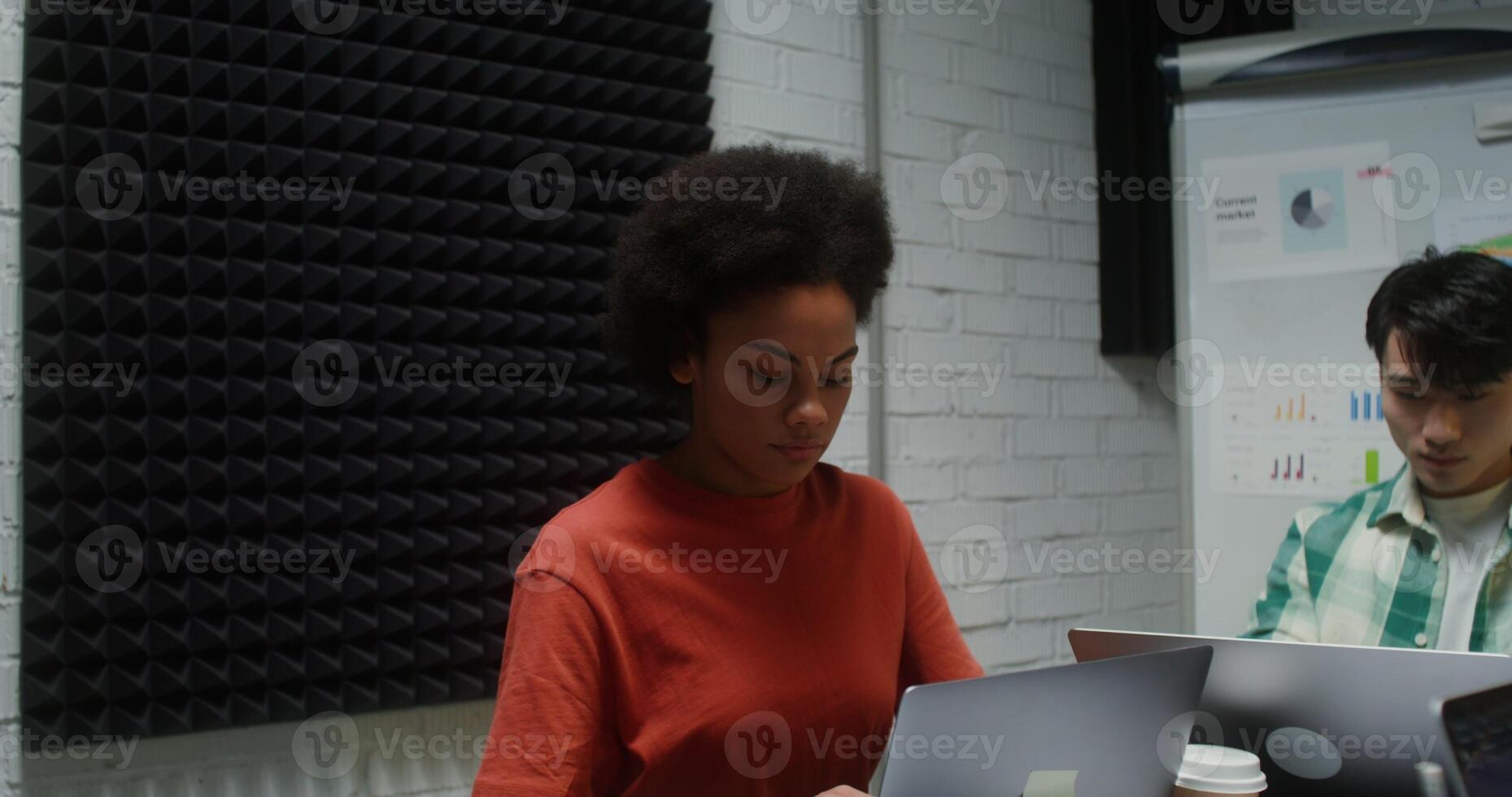 Young woman of African American appearance works at a laptop, periodically looking at her colleagues and participating in a conversation, sitting at a round table in a conference room photo