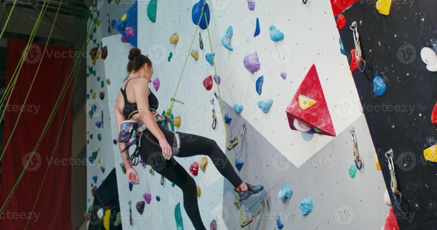 Young woman athlete descends from the climbing wall without using her hands photo