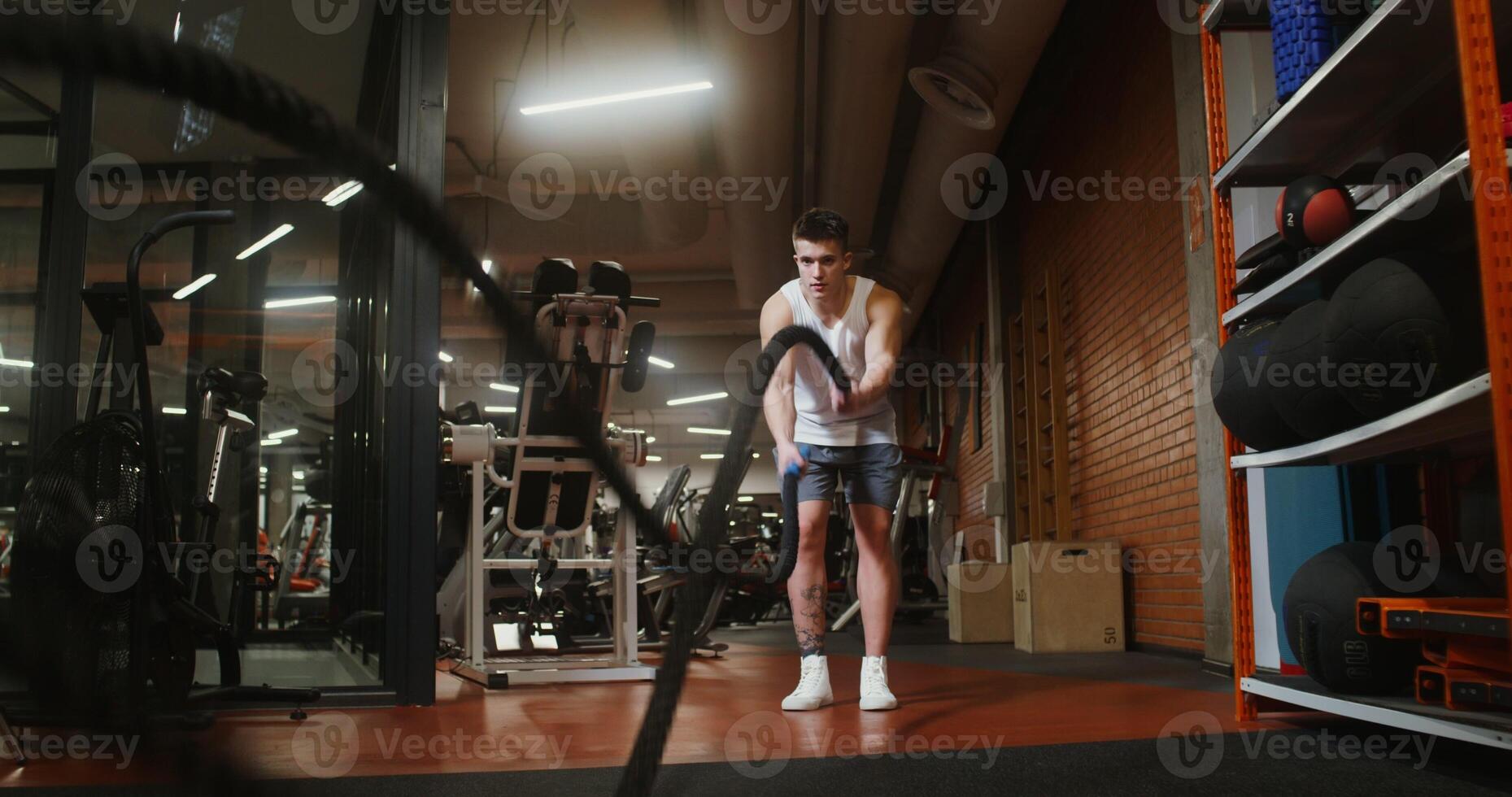 Young muscular man of european appearance uses battle ropes during strength training in modern gym photo