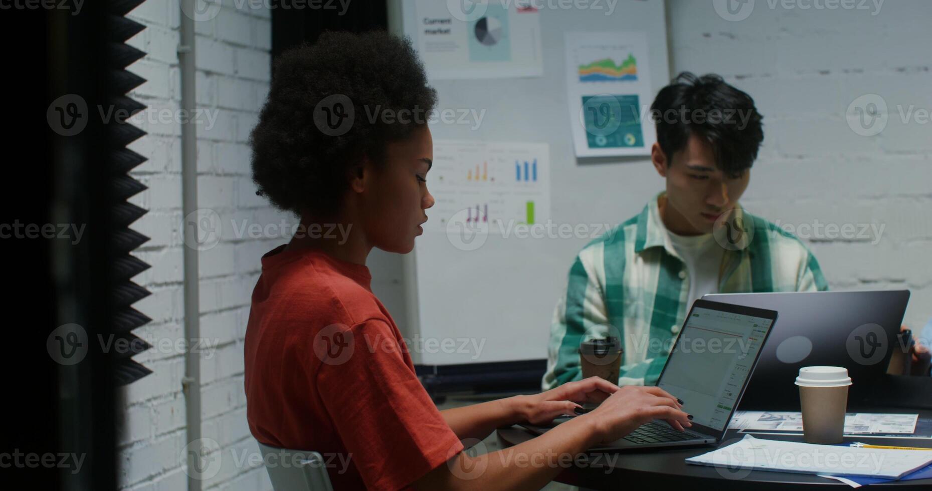 A group of young entrepreneurs of nationalities are enthusiastically working on laptops, sitting at a common table in a meeting room photo