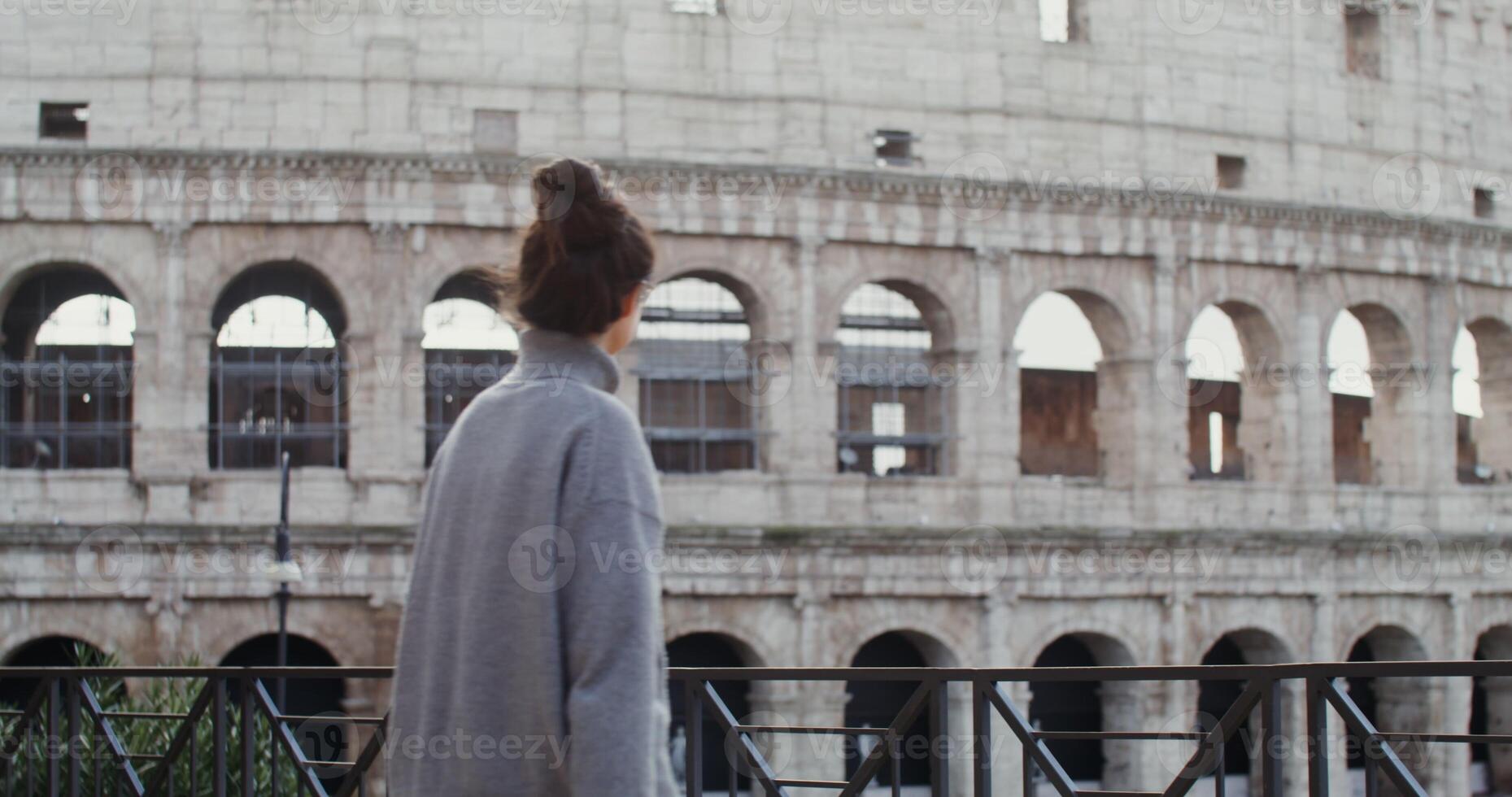 A young beautiful woman smiles while taking photos of the sights of Rome on a mobile phone, standing on an observation deck near the Coliseum. in 4k, red komodo.