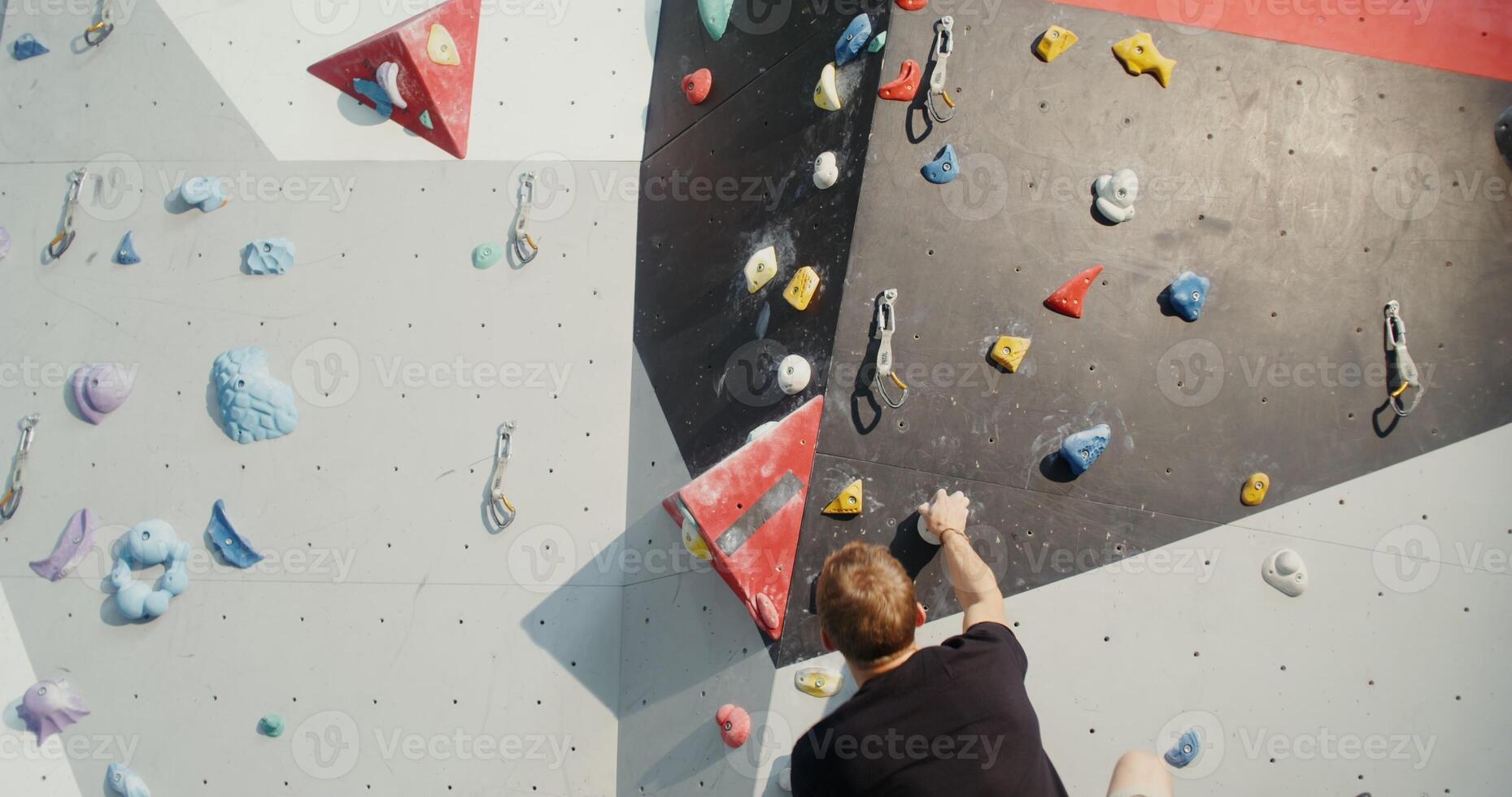 Young man of European appearance in rubberized sports shoes and with a bag of talcum powder climbs up the climbing wall without safety ropes. Preparation of mountaineers in a modern sports hall photo