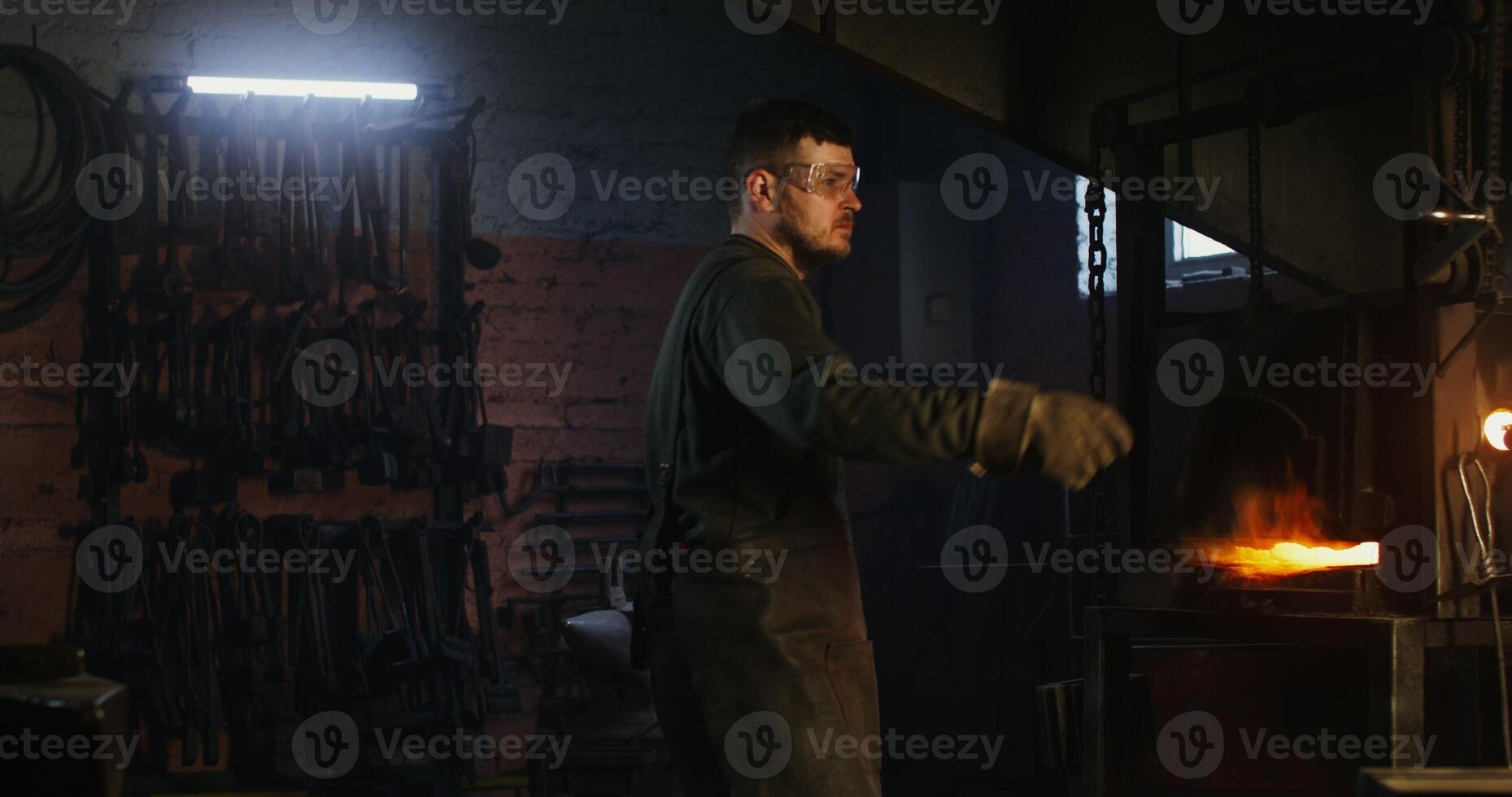 Blacksmith places a metal billet in a burning furnace and, after closing the valve, waits for the iron to melt. Blacksmith workplace, iron forging workflow. 4k , red komodo photo