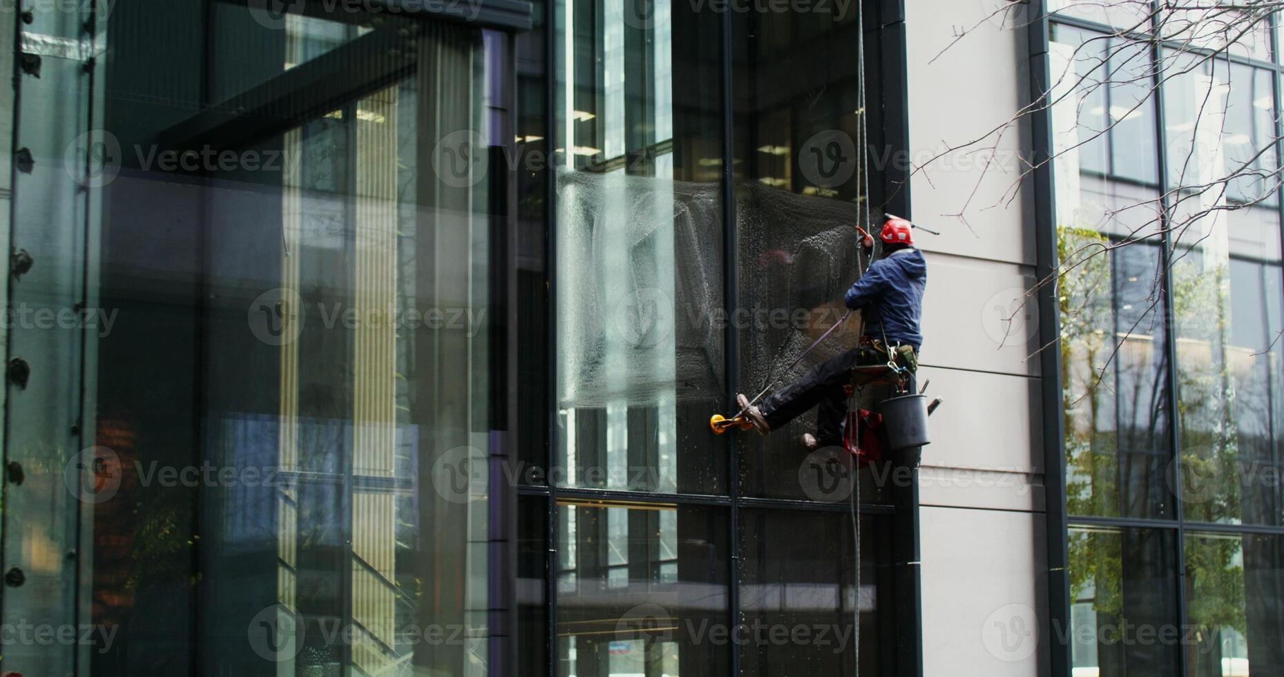 A man in protective gear hanging from safety ropes washes the windows of a skyscraper. in 4k, red komodo photo