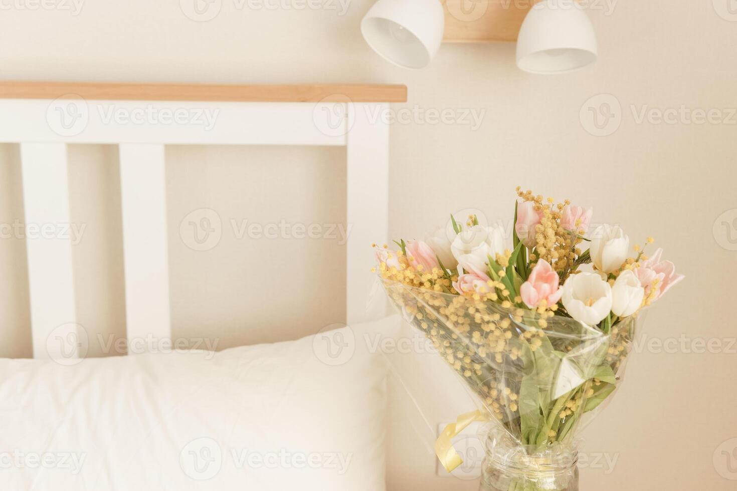 Bouquet of pink and white tulips with mimosa in a glass vase in a bedroom. Spring flower arrangement for interior decoration photo