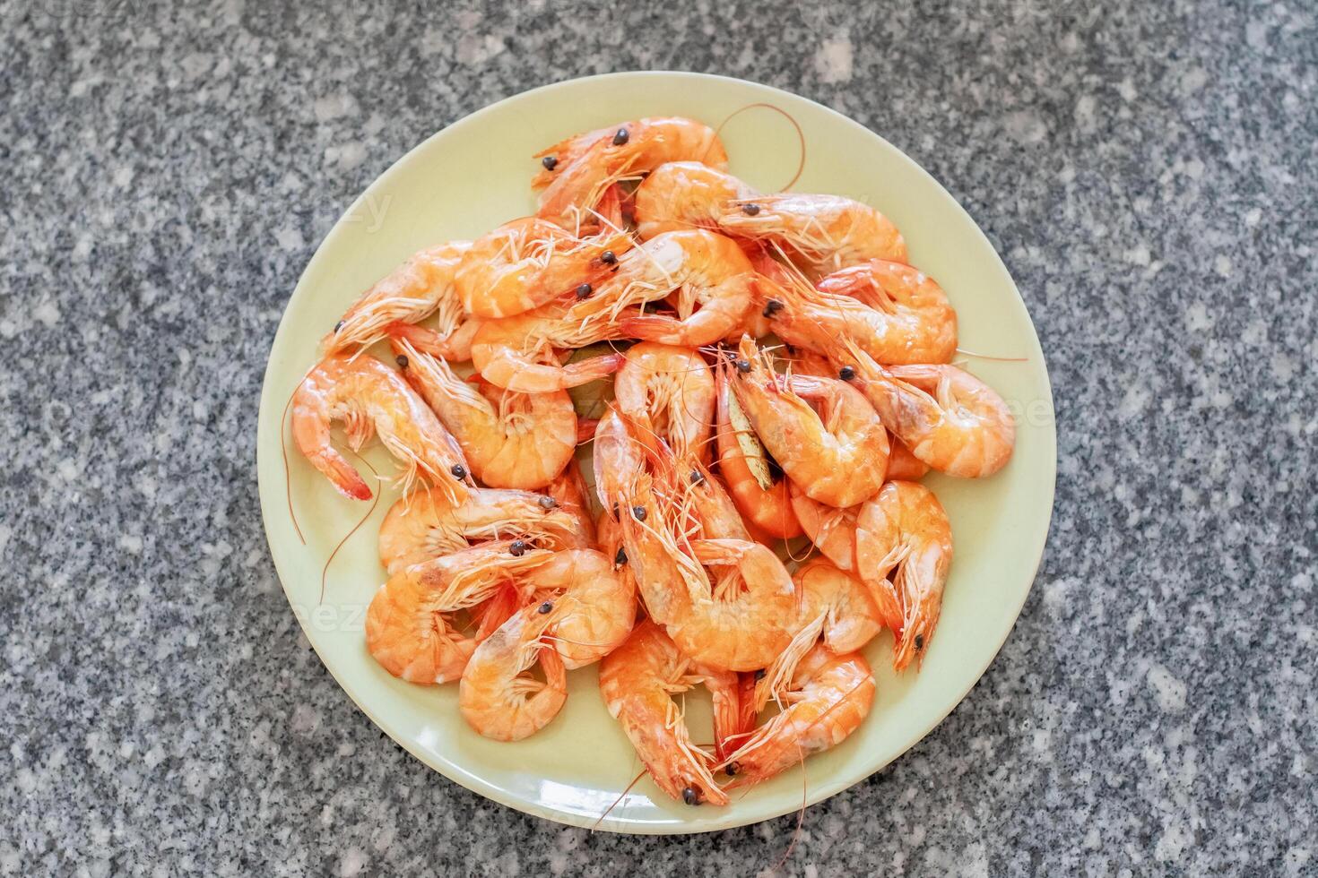 Cooked shrimps are arranged on a light green plate placed on a granite countertop, ready to be enjoyed as a delicious seafood meal or appetizer photo
