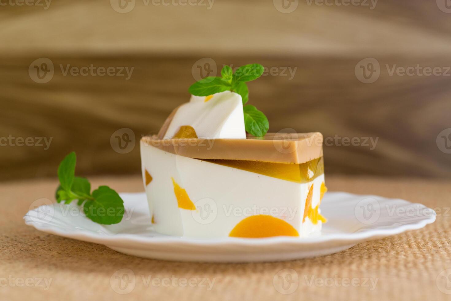 milk jelly dessert with pieces of fruit inside, in a plate on a wooden table. photo