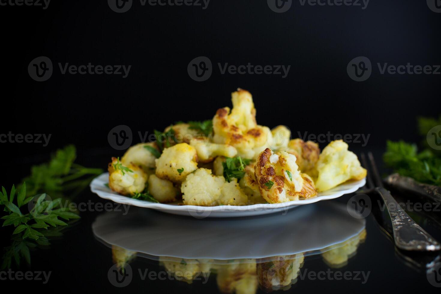 Fried cauliflower with spices and herbs on a black background photo