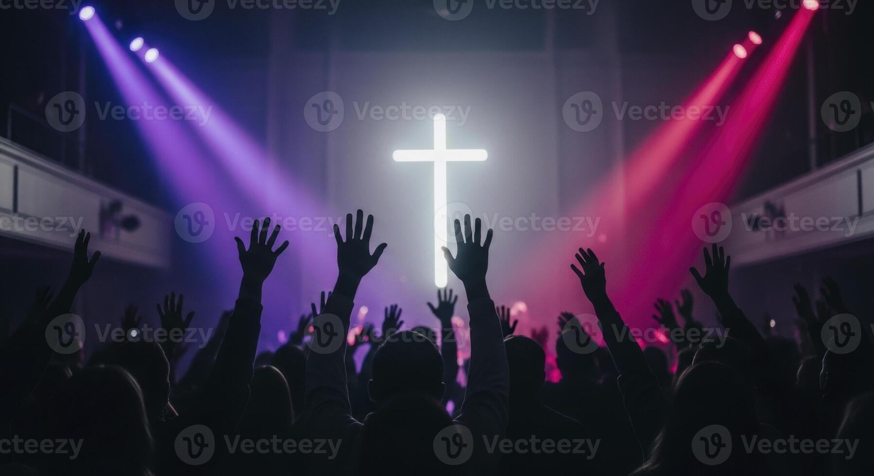 Silhouetted crowd with raised hands worships before a glowing cross under vibrant stage lights photo