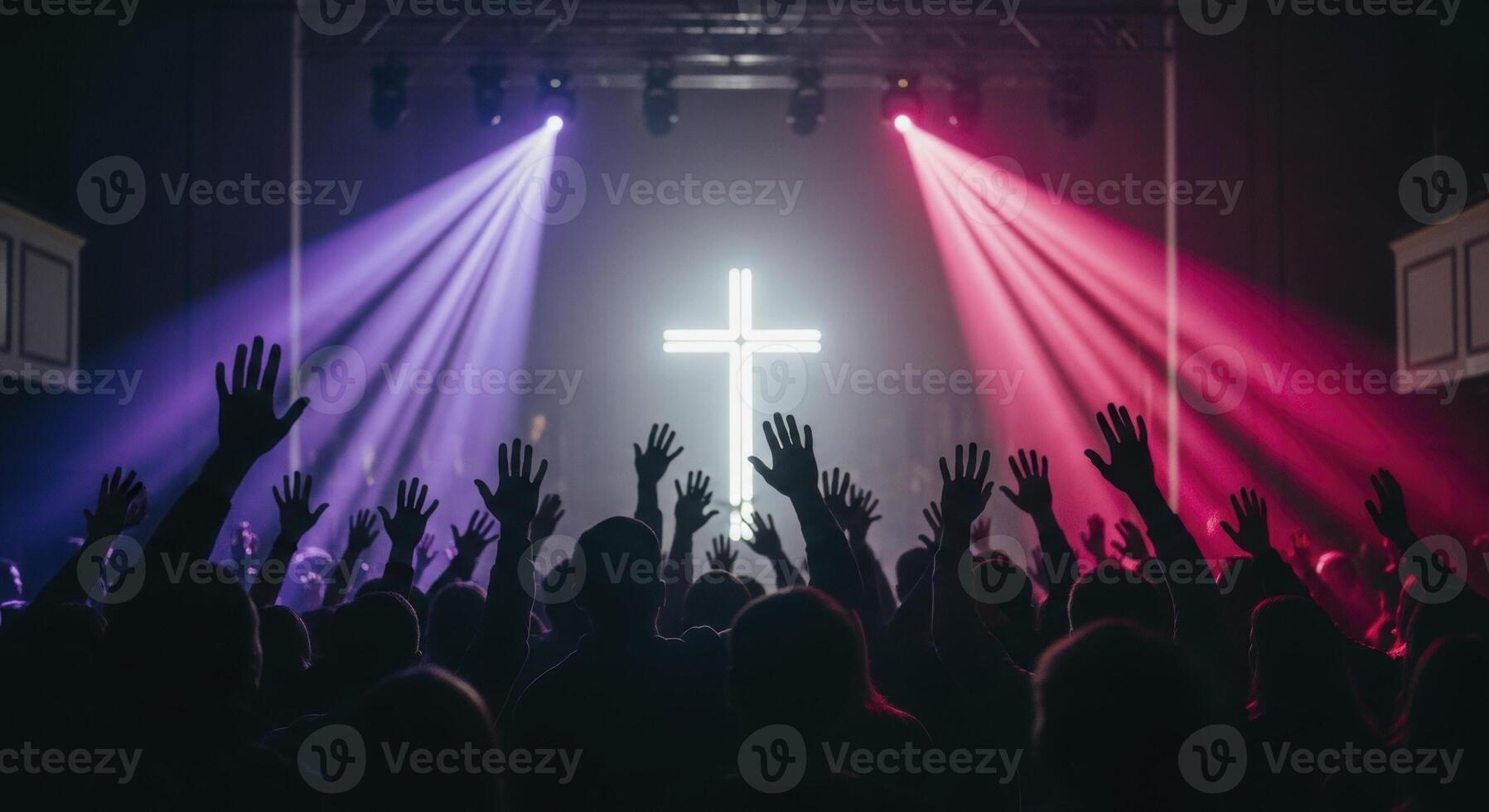 Crowd with raised hands at a worship event, illuminated by purple and pink spotlights and a glowing cross. photo