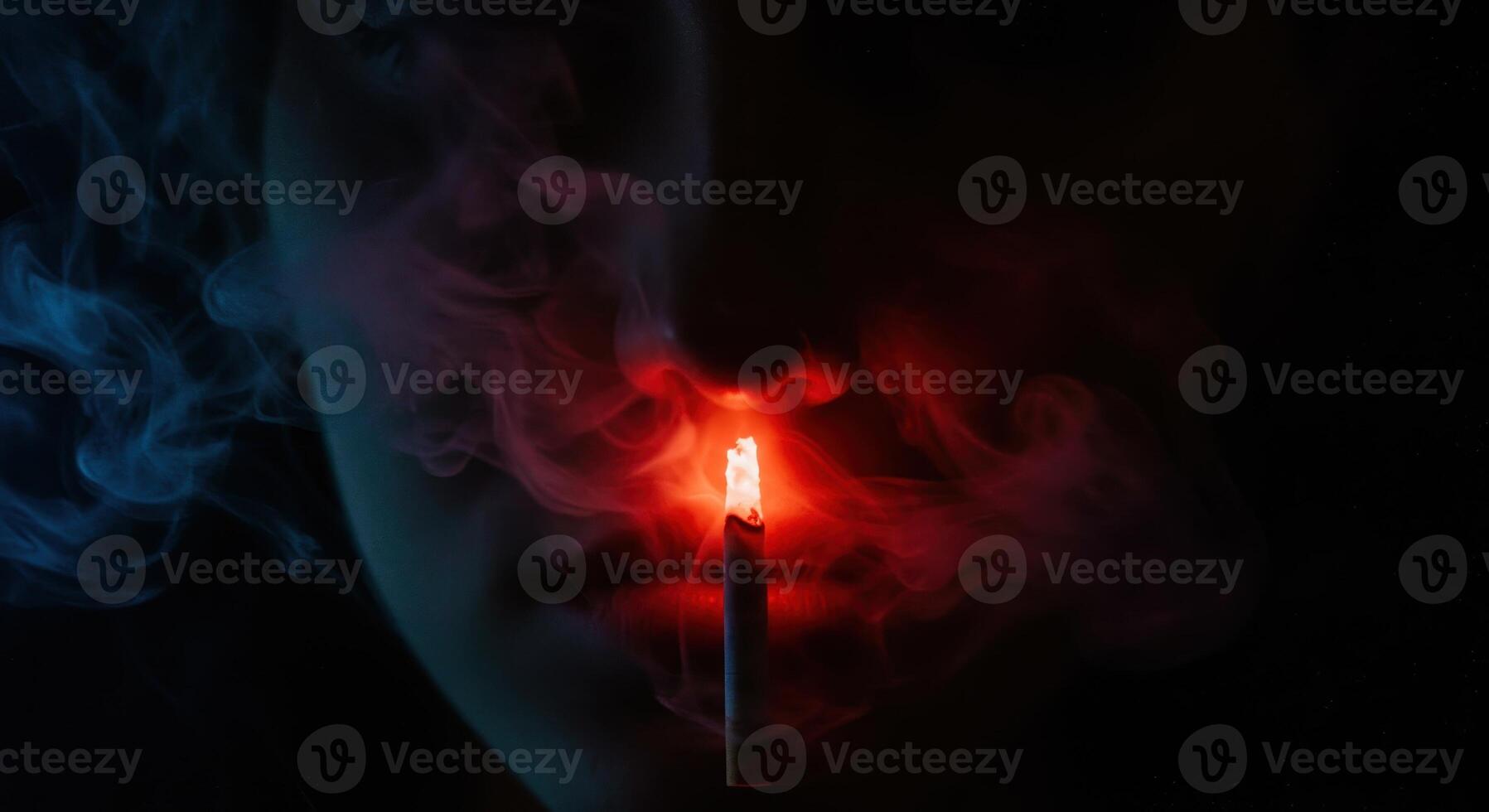 Glowing cigarette tip with red and blue smoke illuminating a shadowy figure in darkness. photo