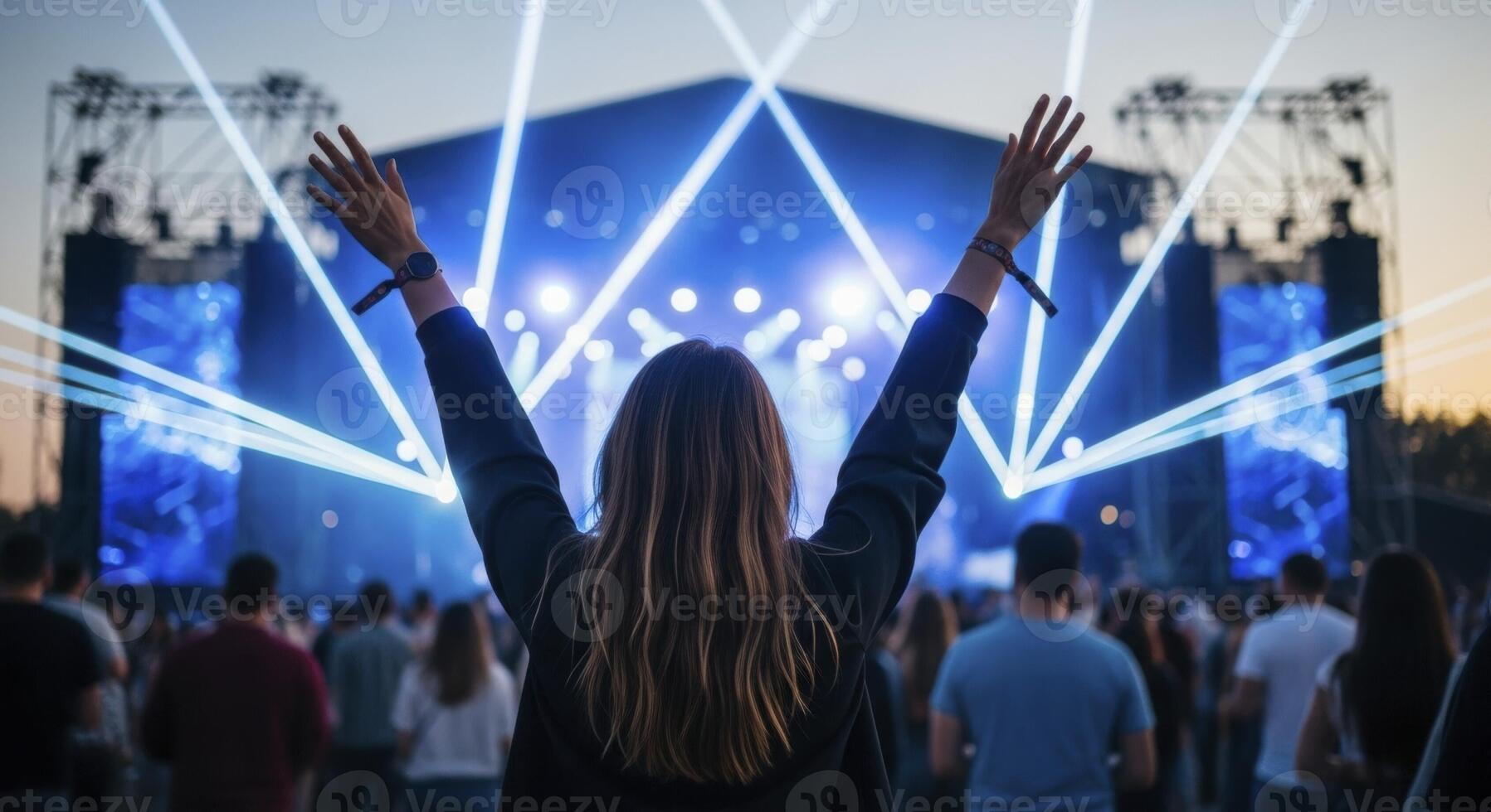 Young woman celebrating at an outdoor music concert with bright stage lights and a large crowd. photo