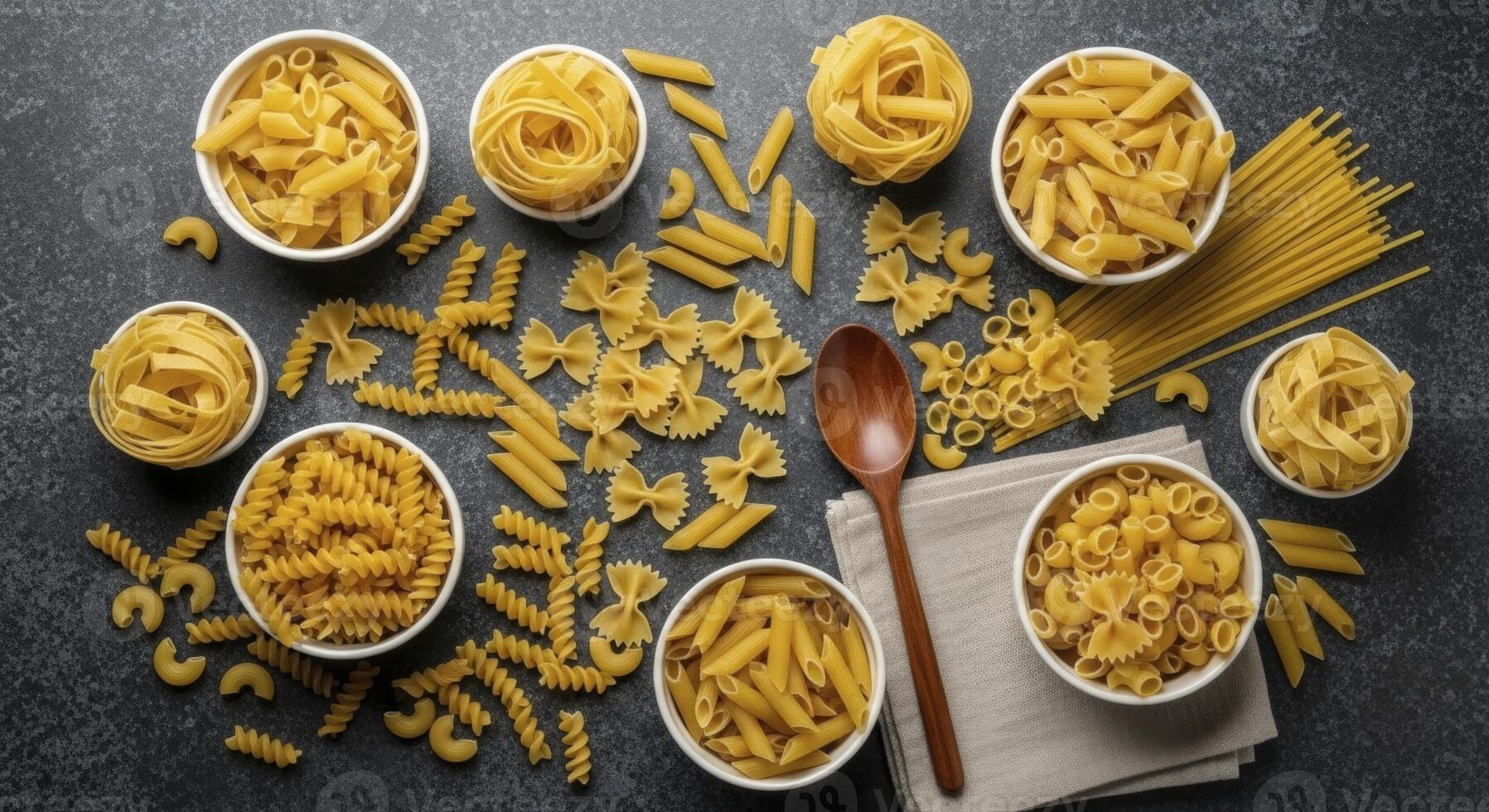 Assortment of dry pasta shapes including fusilli, penne, farfalle, and spaghetti on a dark surface photo