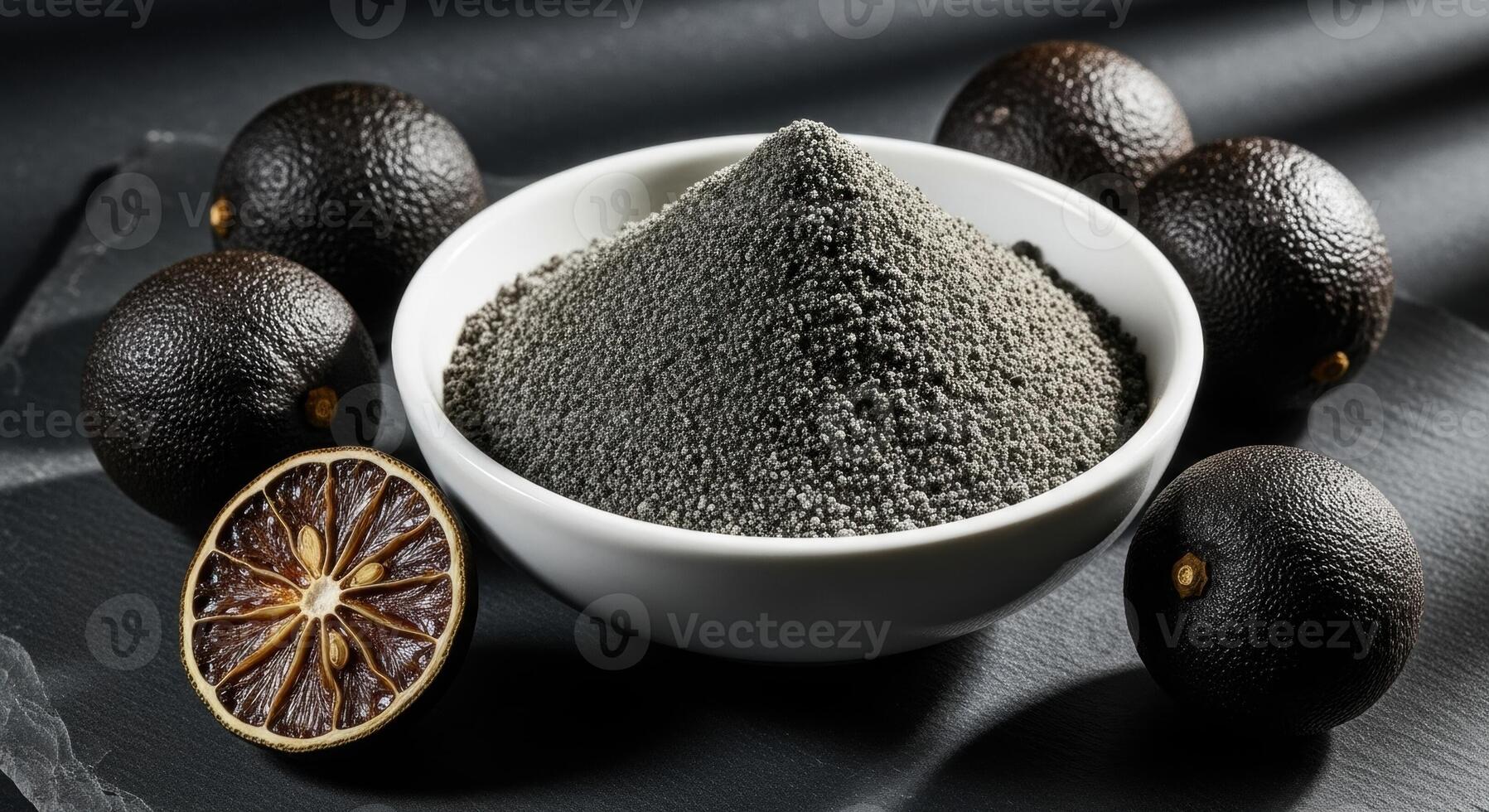 Black lime powder in a white bowl with whole and sliced dried limes on a dark surface. photo
