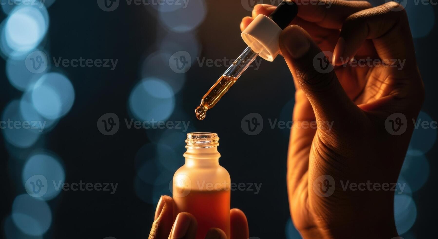 Dark skinned hand holding a dropper bottle with a drop of amber liquid photo