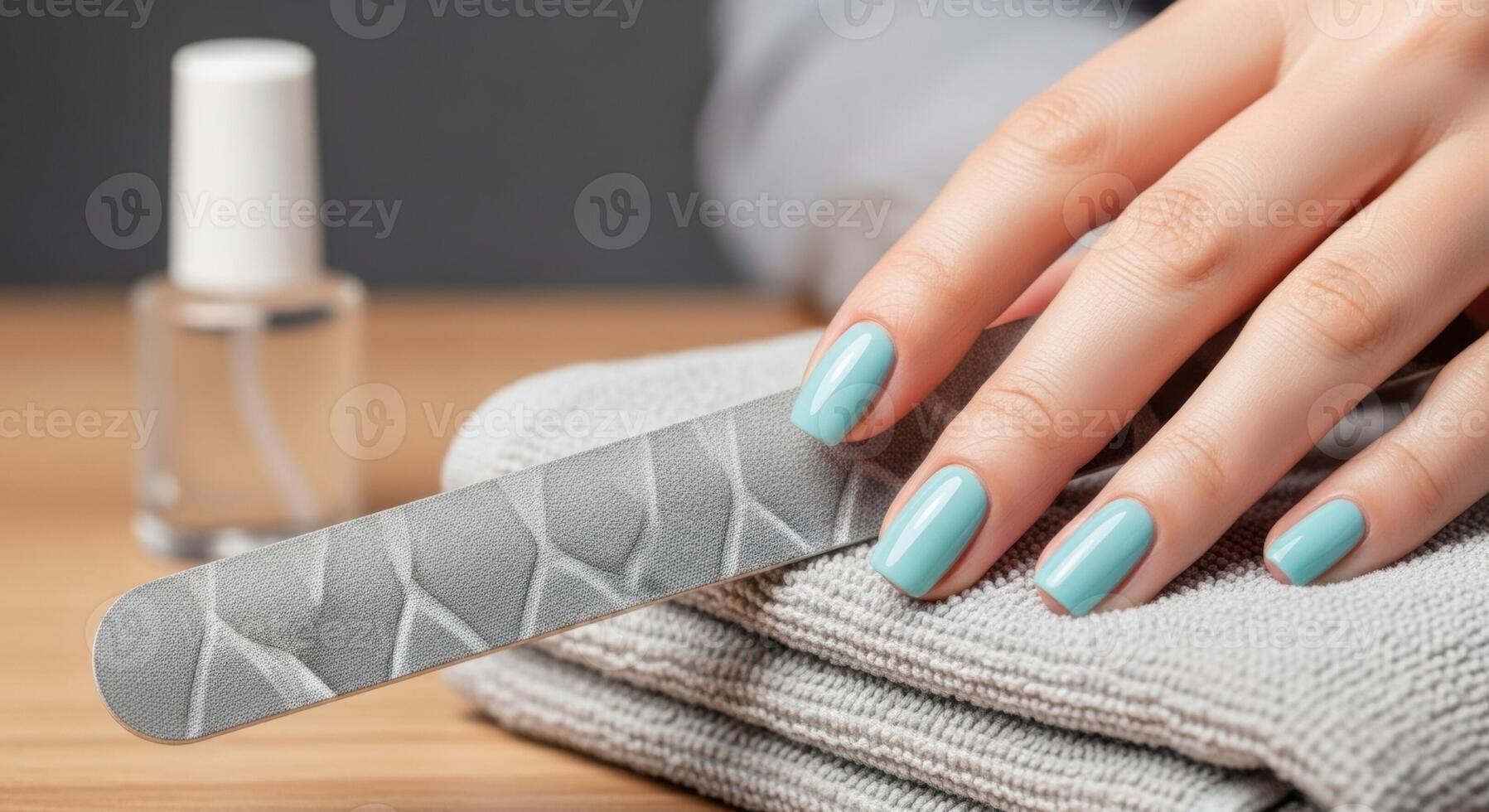 Woman Hand with Light Blue Manicured Nails and Nail File on Grey Towel photo