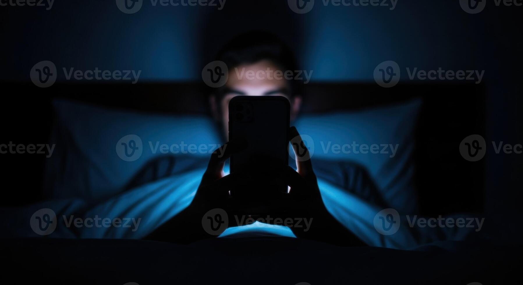 Man using smartphone in bed at night with blue screen light illuminating his face photo