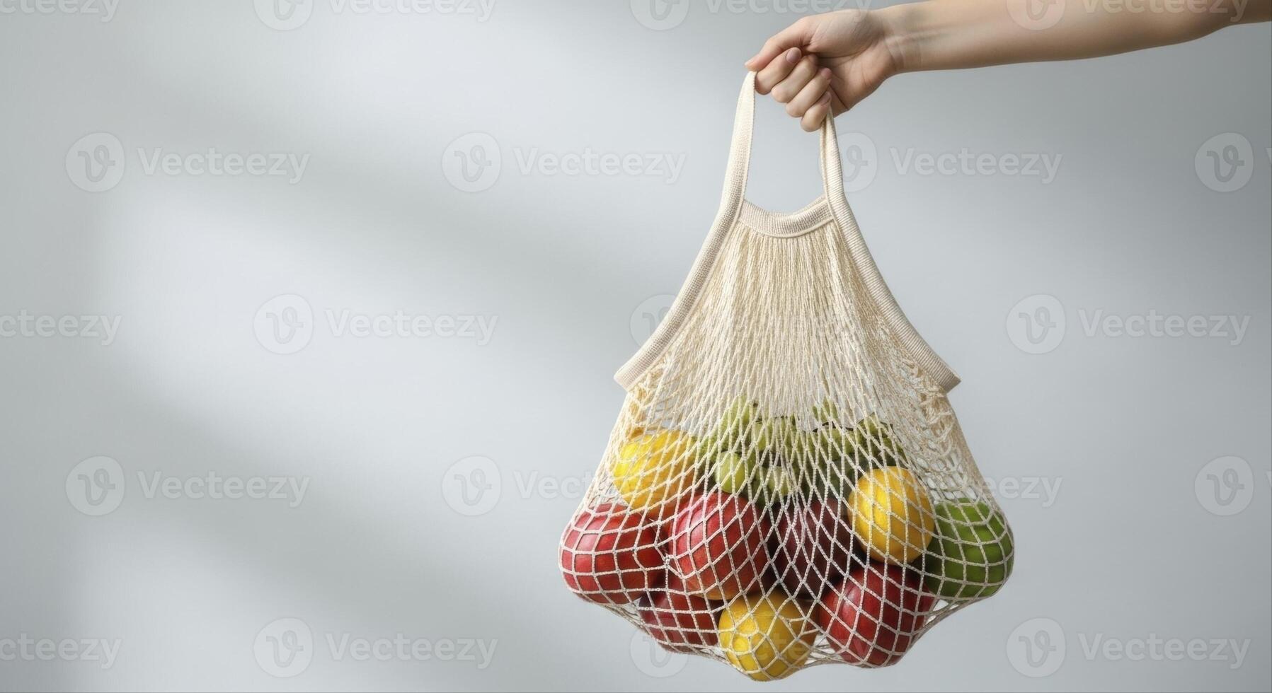 Hand holding a beige woven mesh grocery bag filled with fresh fruit for eco friendly shopping photo