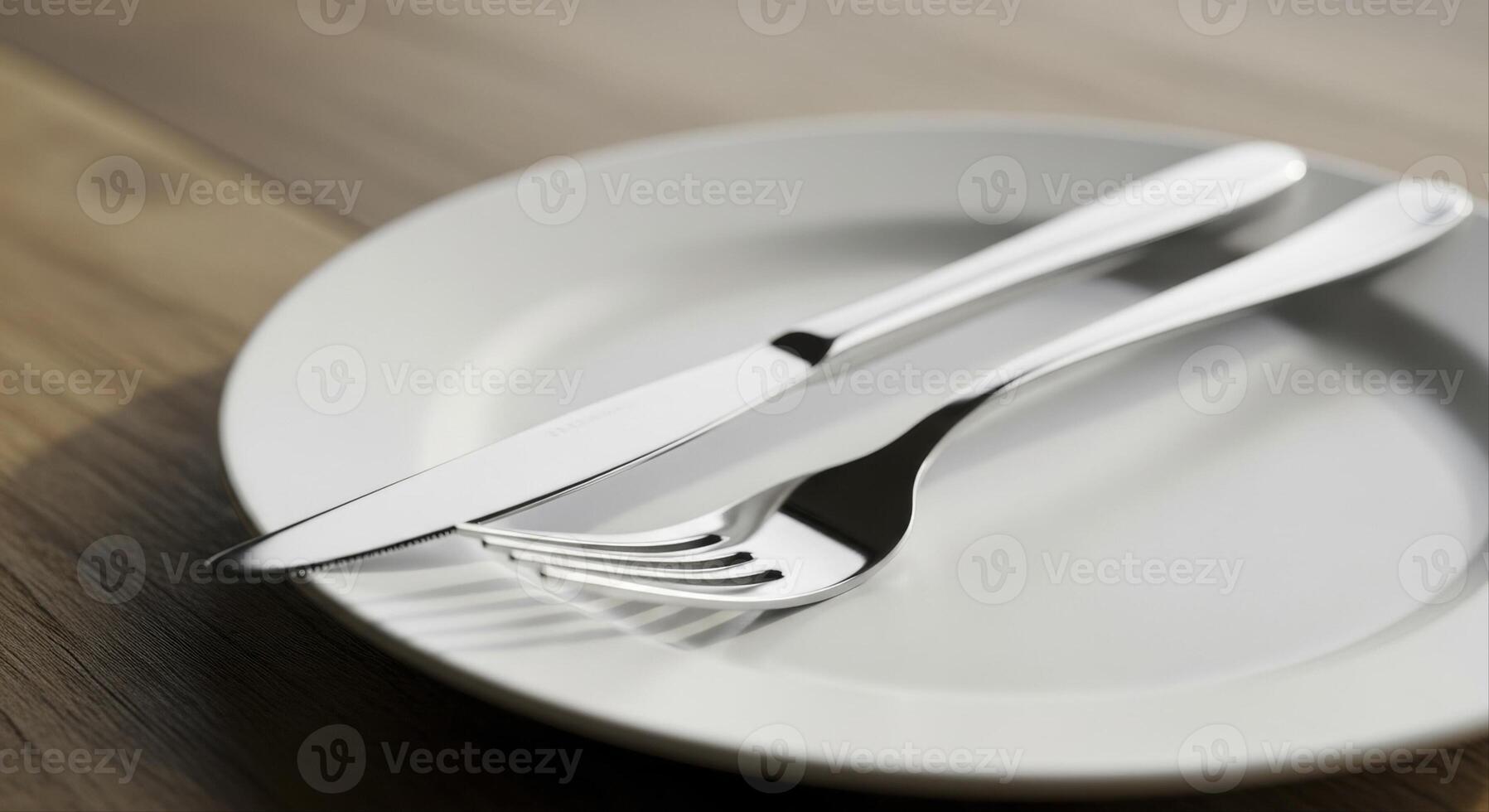 Polished stainless steel fork and knife on a white plate set on a wooden table photo