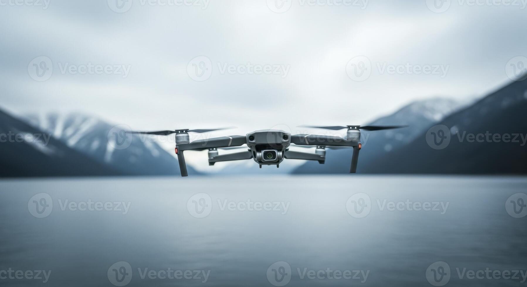 Grey quadcopter drone flying over a calm lake with snow capped mountains photo