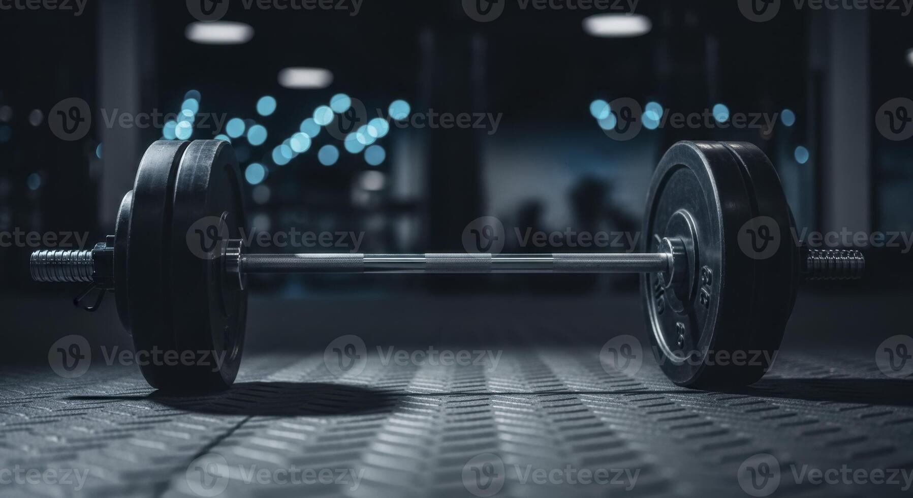 Heavy barbell with dark weight plates on a textured gym floor in a dimly lit fitness center photo