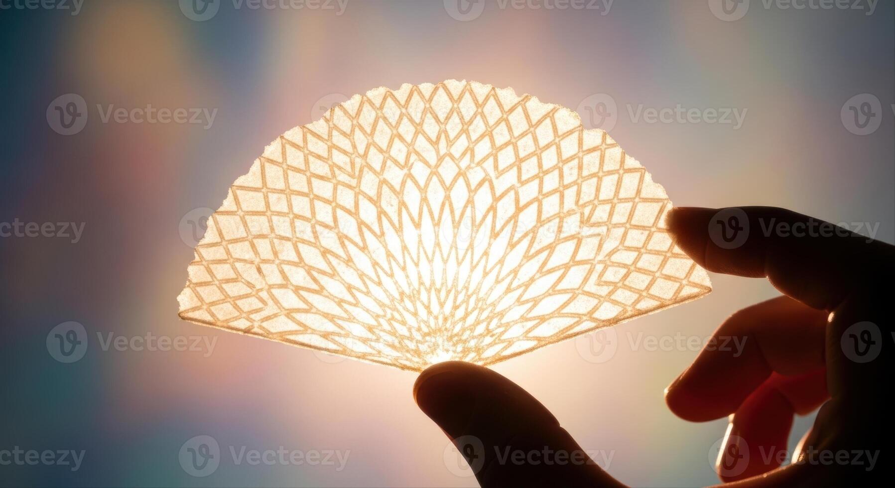 Hand holding a delicate translucent fan shaped wafer with intricate geometric pattern photo