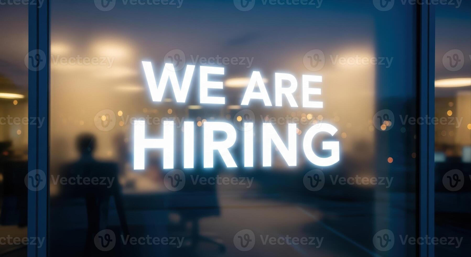 Vibrant 'WE ARE HIRING' message glowing on a modern office building window at night photo