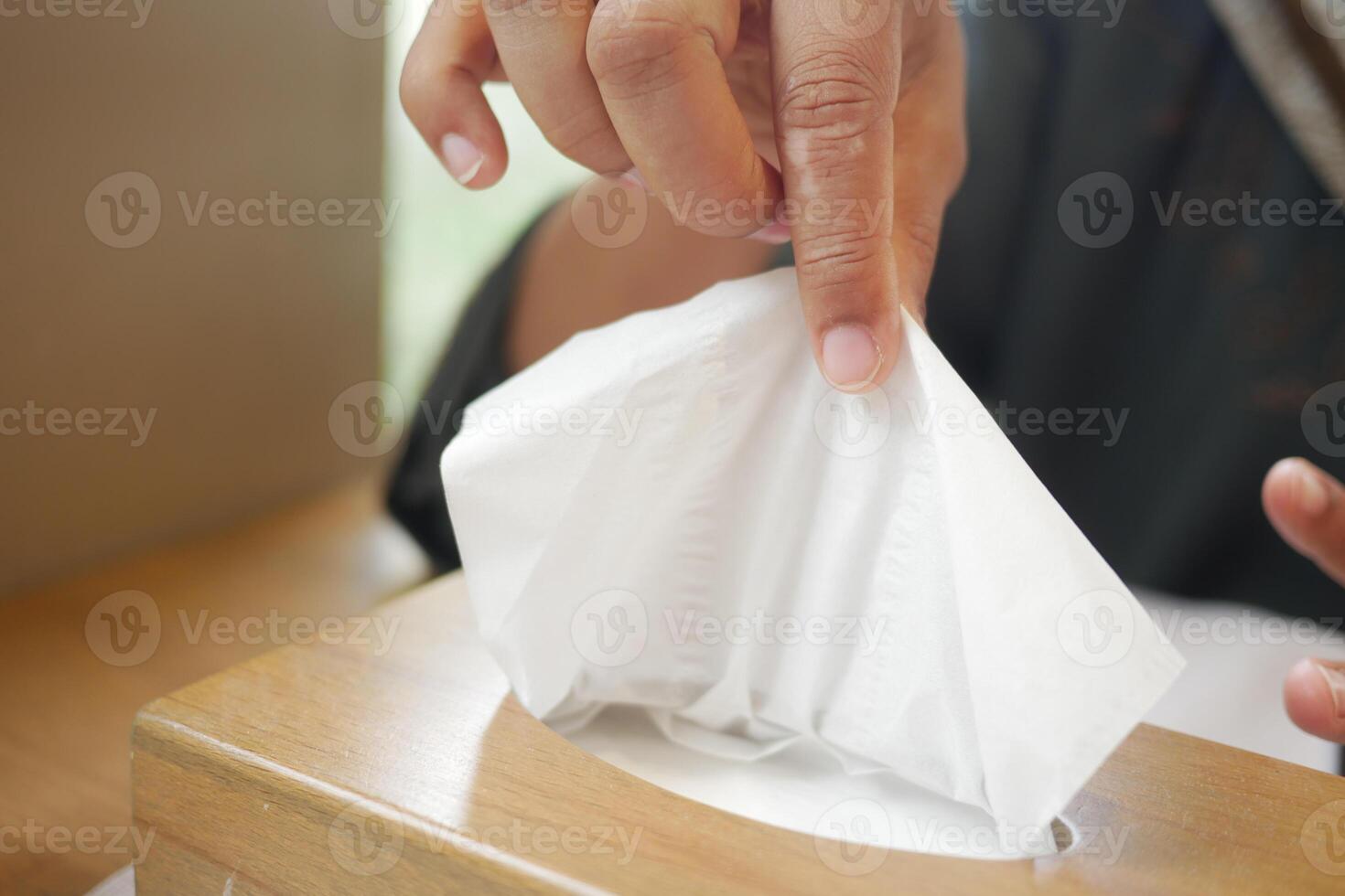 Person taking tissue from a wooden tissue box indoors photo