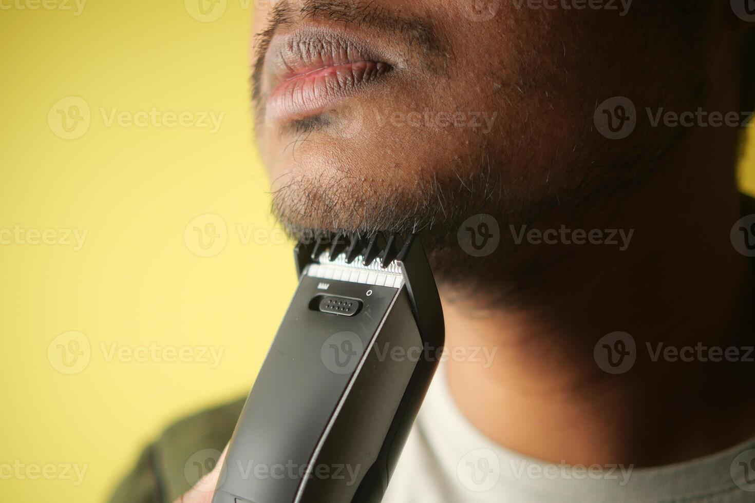 Man trims his beard with an electric trimmer indoors photo