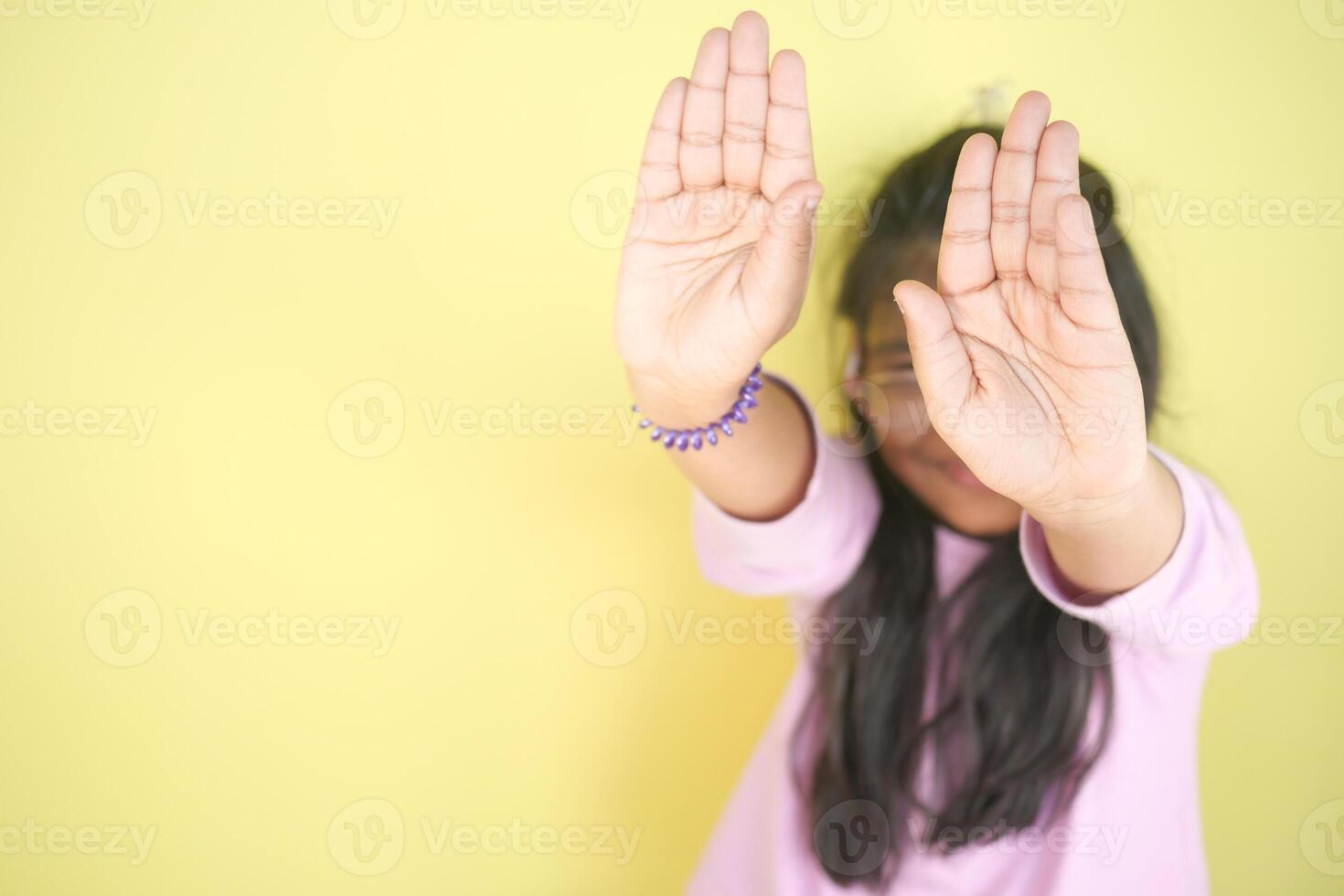 Child playfully posing with hands up against yellow photo