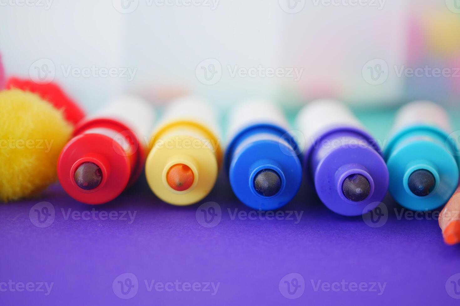 Colorful markers arranged in a row on a purple surface photo