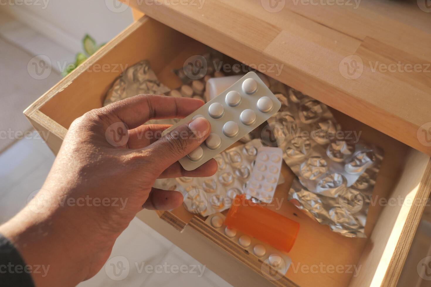 Hand with pill pack over messy medication drawer photo