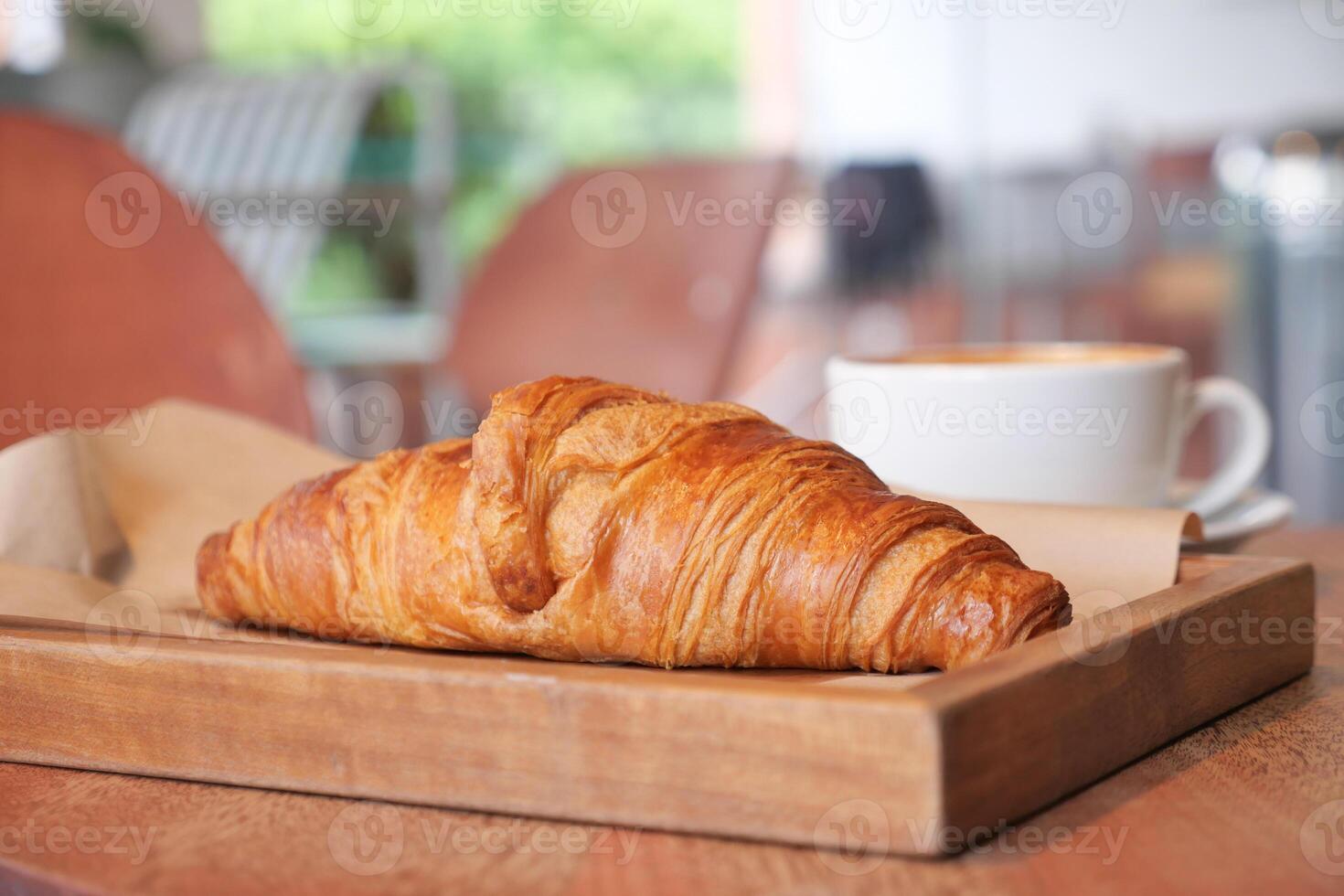 Delicious croissant with coffee on a wooden tray in cafe photo