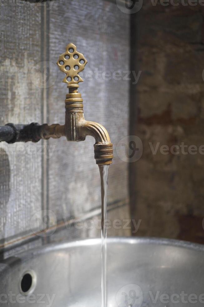 Water flowing from an old brass faucet in a rustic setting photo
